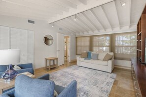 A spacious living room with a white ceiling, a white sofa, a blue armchair, and a wooden coffee table.