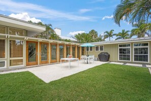 A modern house with a covered patio, a lawn, and a grill.