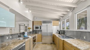 A modern kitchen with granite countertops, stainless steel appliances, and a view of the outdoors through large windows.