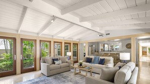 A spacious living room with a high ceiling, large windows, and a view of greenery outside.