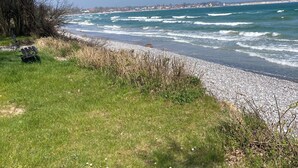 Une vue sur la côte, avec une zone herbeuse, une plage de galets et un ciel bleu dégagé.