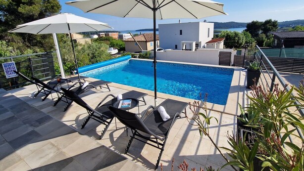 A poolside area with lounge chairs and umbrellas, a clear view of the pool, and a building in the background.