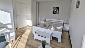 A modern bedroom with a bed, bedside tables, a small table with a plant, and a door.