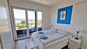 A bedroom with a bed, a nightstand, a bench, and a view of a balcony with a table and chairs.