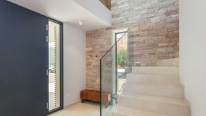 A modern interior with a stone wall, a glass railing, and a bench near a staircase.