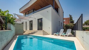 A modern two-story house with a swimming pool and outdoor seating.