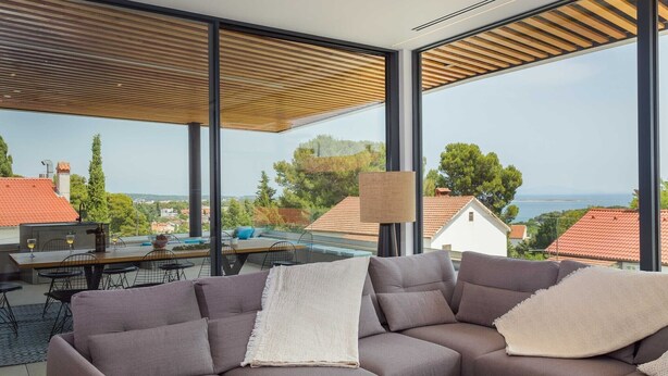 A modern living room with a large window, a sofa, a table with chairs, and a lamp.
