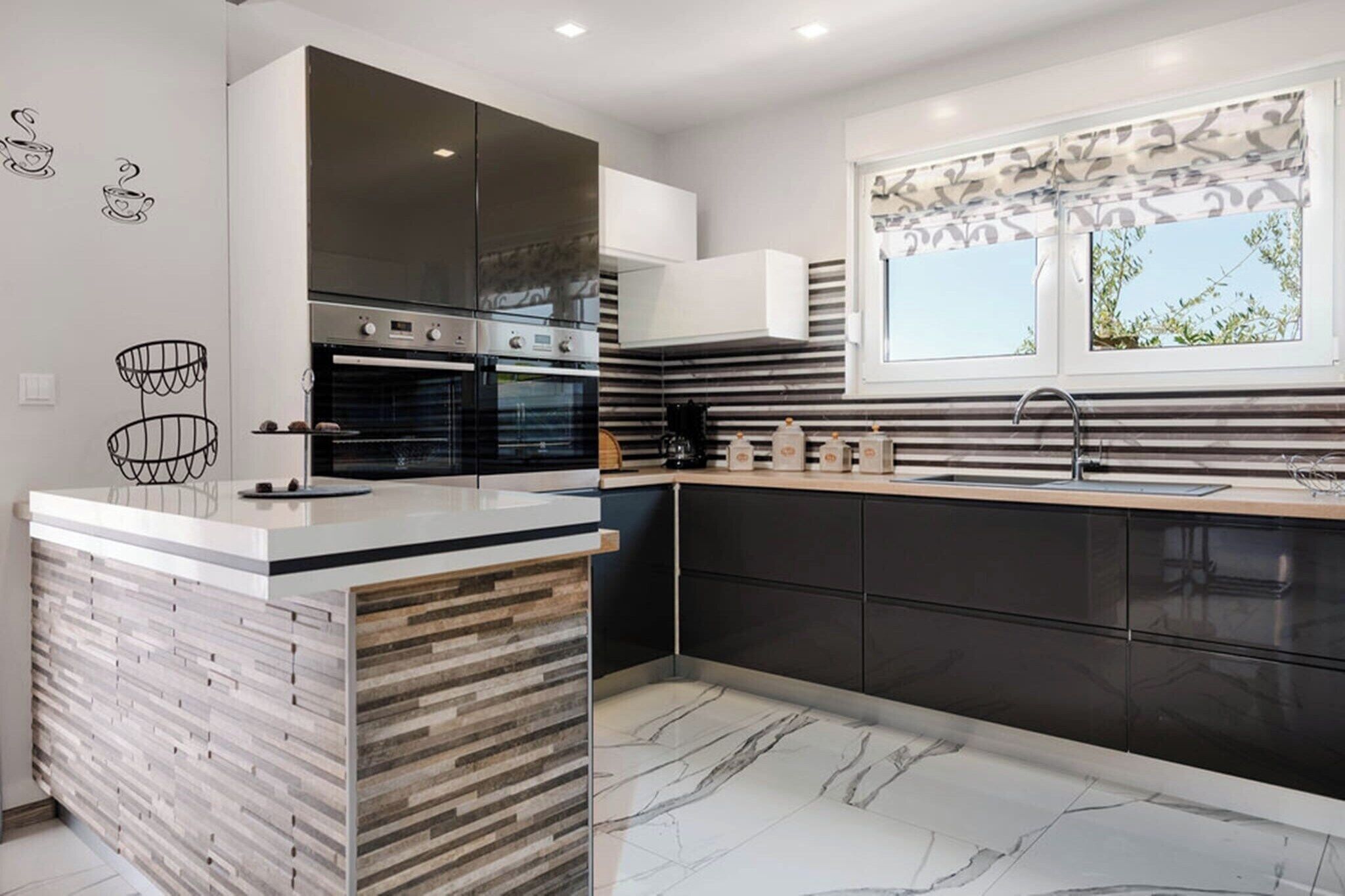 Una cocina moderna con una isla central, hornos integrados y un ventanal con vistas.