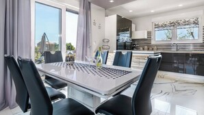 Un comedor moderno con una mesa de vidrio y sillas negras, una cocina con electrodomésticos de acero inoxidable, y vistas al exterior.