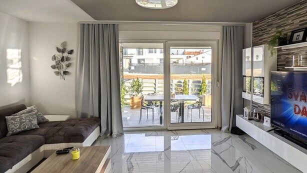Una sala moderna con un sofá, una mesa de centro, un televisor de pantalla plana y un ventanal corredizo que da a un patio exterior.