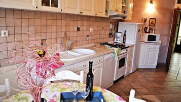 A kitchen with white cabinets, a sink, a stove, and a microwave. There is a vase with pink flowers on the counter.