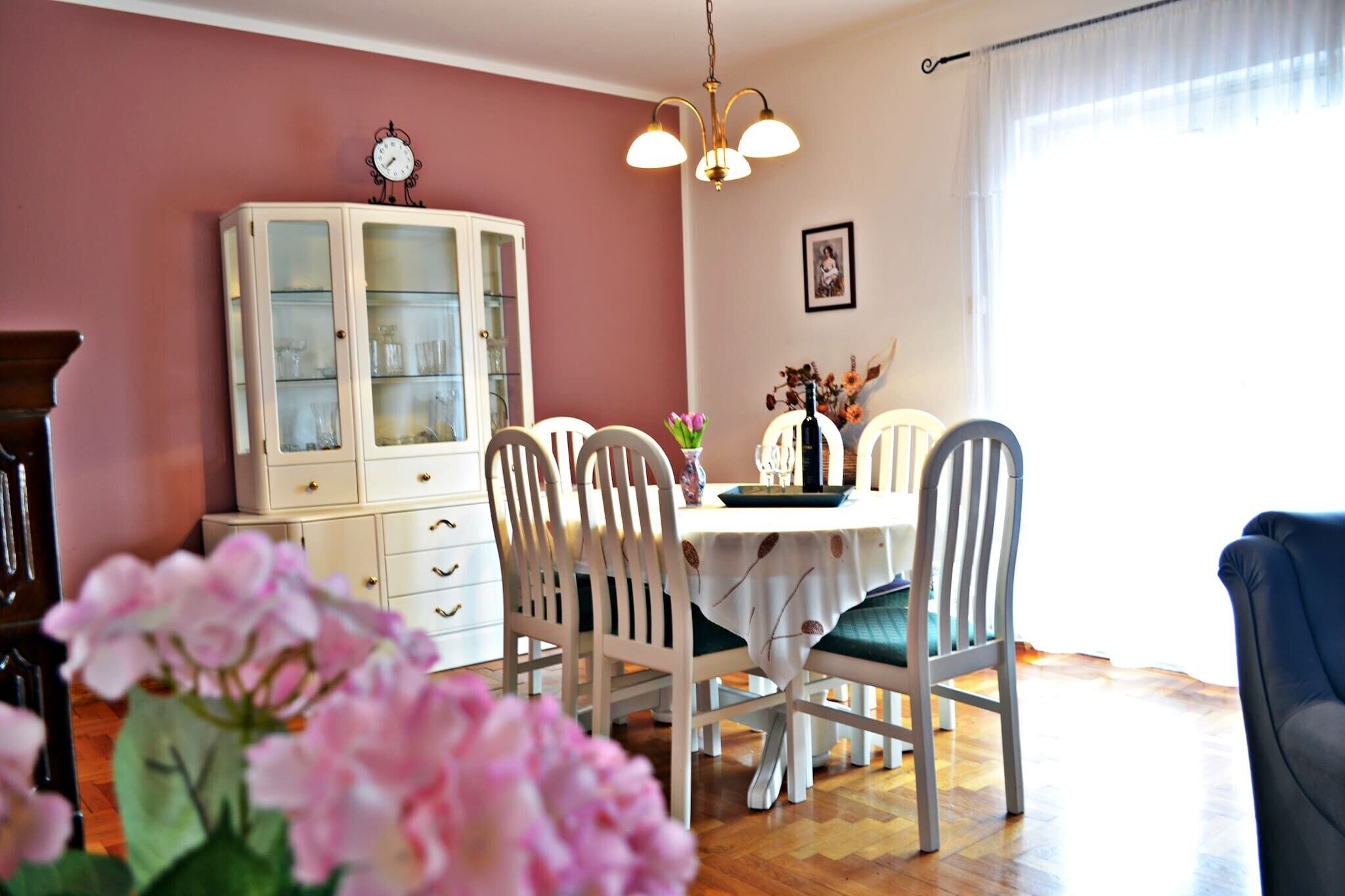 A dining area with a white table, four chairs, a white cabinet, and a clock on the wall.