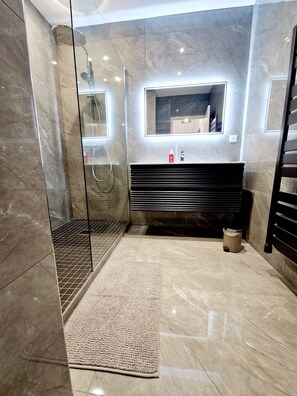 Features a sleek design with a large mirror, glass-enclosed shower, and textured rug.
