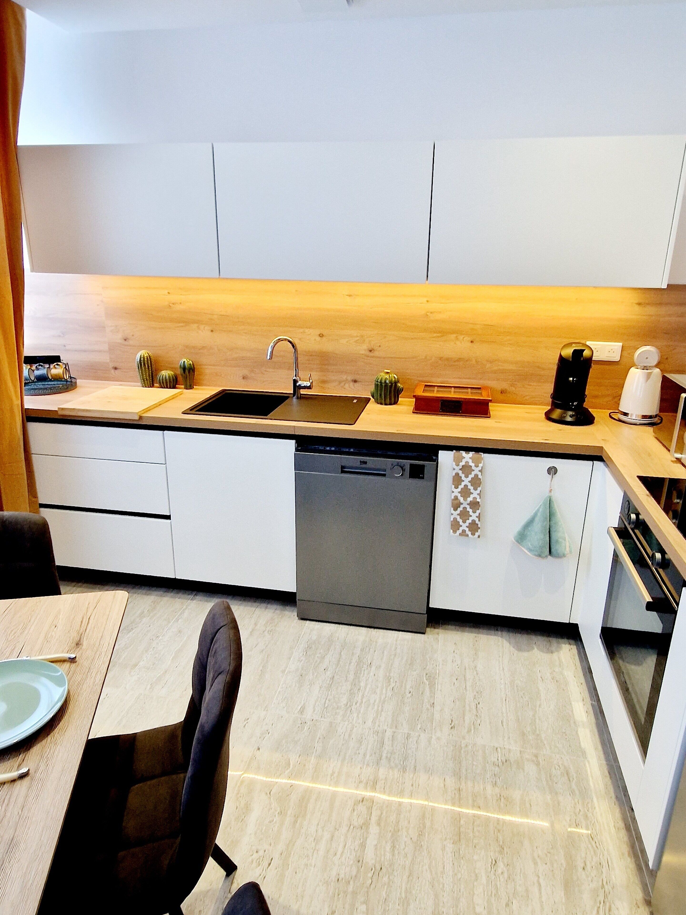 A modern kitchen with a wooden countertop, a dishwasher, and a sink. There are decorative items on the counter and a towel hanging on the oven door.