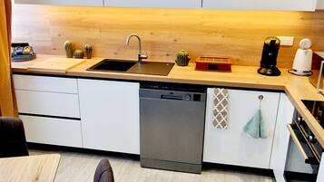 A modern kitchen with a wooden countertop, a dishwasher, and a sink. There are decorative items on the counter and a towel hanging on the oven door.