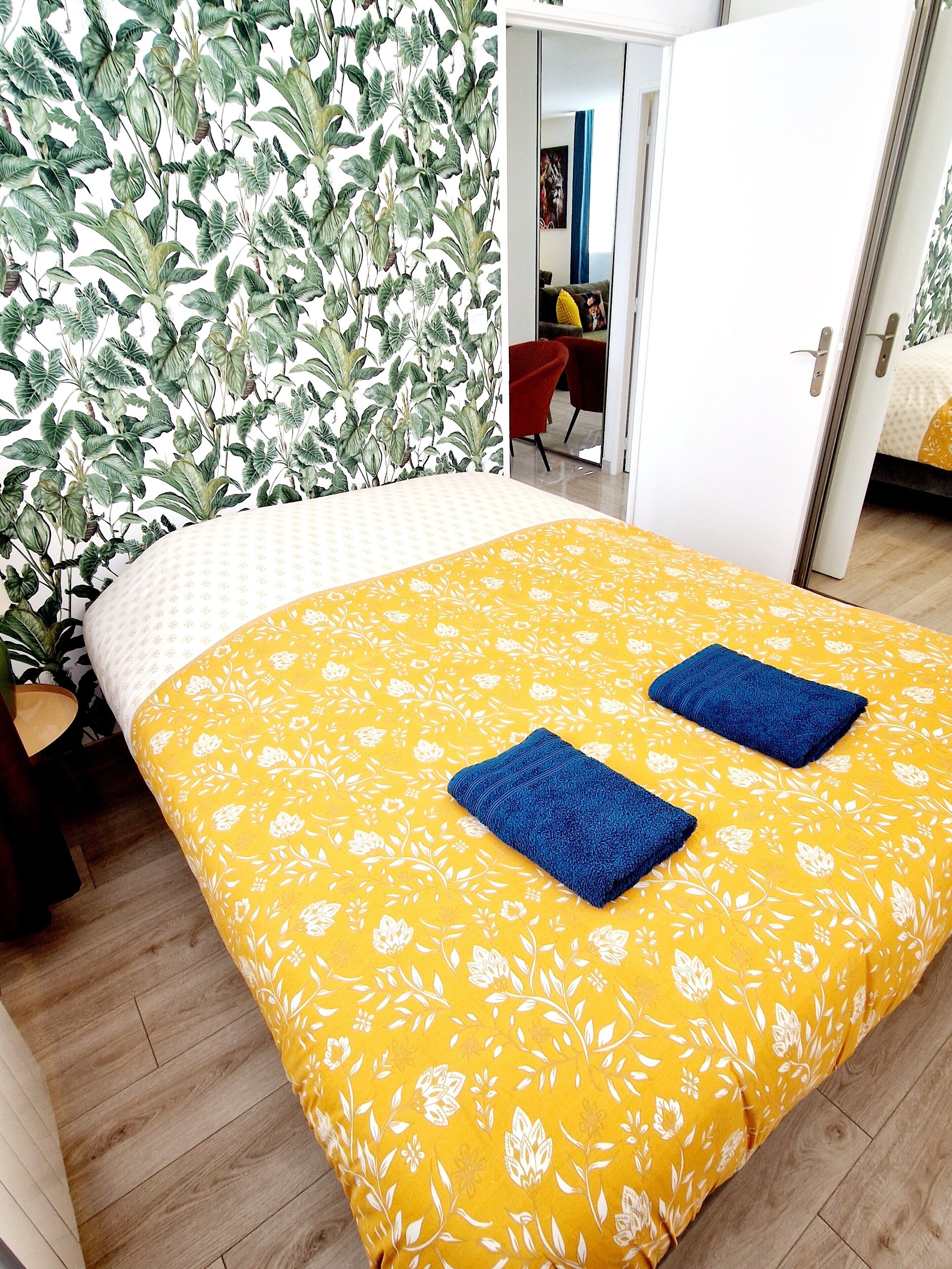 A room with a bed, a wall with a leafy pattern, and a door leading to another room.