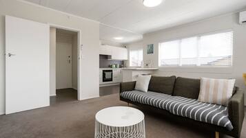 A modern living room with a sofa, a round white table, and a kitchen in the background.