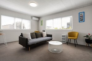 Una sala de estar moderna con un sofá, una mesa de centro redonda, un sillón amarillo y una planta en maceta.