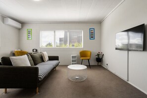 A modern living room with a sofa, a round coffee table, and a TV mounted on the wall. - Bunker 1:  "Urban meets Rustic" (Te Awamutu)