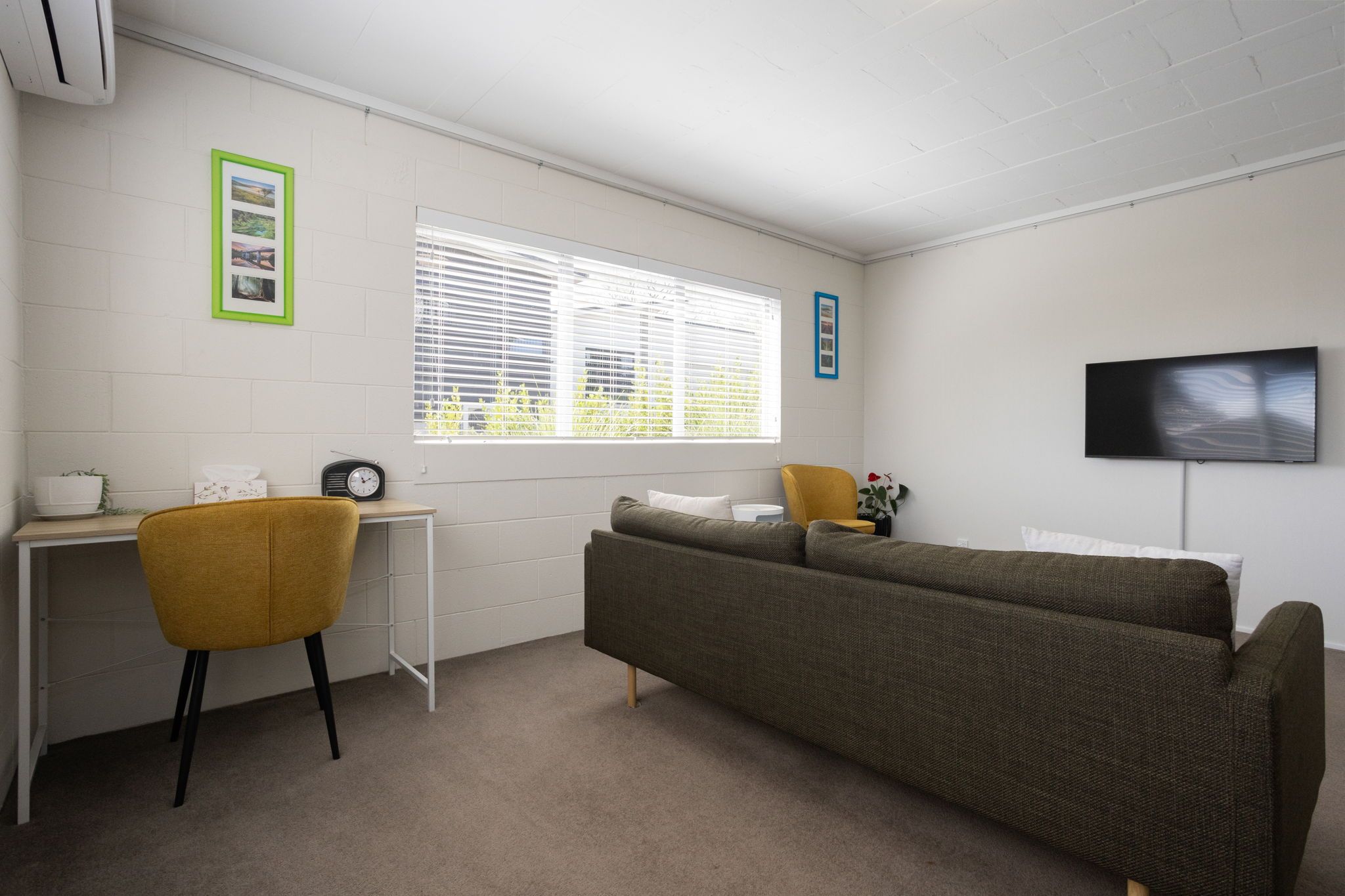 A room with a sofa, a chair, a small table, a TV, and a window with blinds.