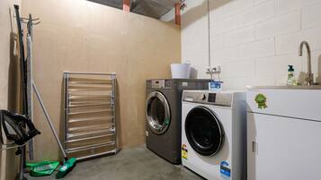 A laundry room with two washing machines, a drying rack, and a sink with a faucet.