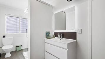 Un baño moderno con inodoro blanco, un lavabo con espejo y un cubo de basura verde.