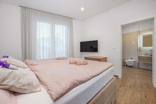 A hotel room with a bed, a TV, a bathroom with a mirror, and a window with curtains.