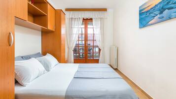 Un dormitorio con cama, armario de madera y vistas a través de una ventana con cortinas.