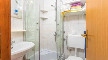 Un baño moderno con ducha de vidrio, lavamanos blanco y un inodoro.