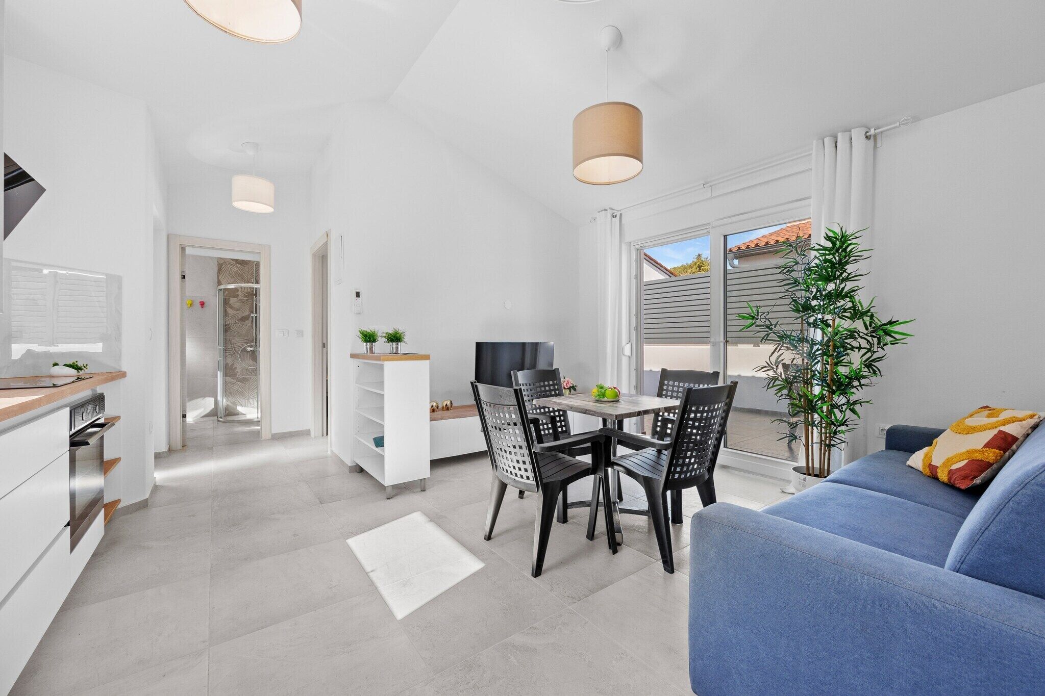 A modern kitchen with white cabinets, a dining area with a table and chairs, and a blue sofa with a cushion.