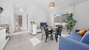 Eine moderne Küche mit weißen Schränken, ein Essbereich mit Tisch und Stühlen sowie ein blaues Sofa mit Kissen.