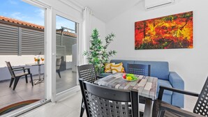 Ein modernes Wohnzimmer mit einem blauen Sofa, einem Esstisch mit Stühlen, einer Topfpflanze und einem farbenfrohen, abstrakten Gemälde an der Wand.