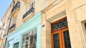 Un bâtiment à la façade bleu clair, une porte en bois ornée de motifs métalliques complexes et un balcon avec des balustrades noires.