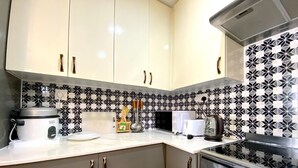 Une cuisine avec des meubles blancs, un dosseret carrelé noir et blanc, une cuisinière et un autocuiseur.