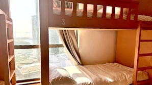 Une chambre avec un lit superposé, une vue sur la ville, une fenêtre et une échelle en bois.