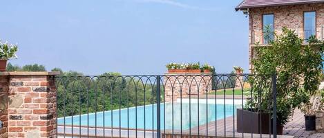 A swimming pool with a brick wall and a metal fence, surrounded by greenery and a clear sky.