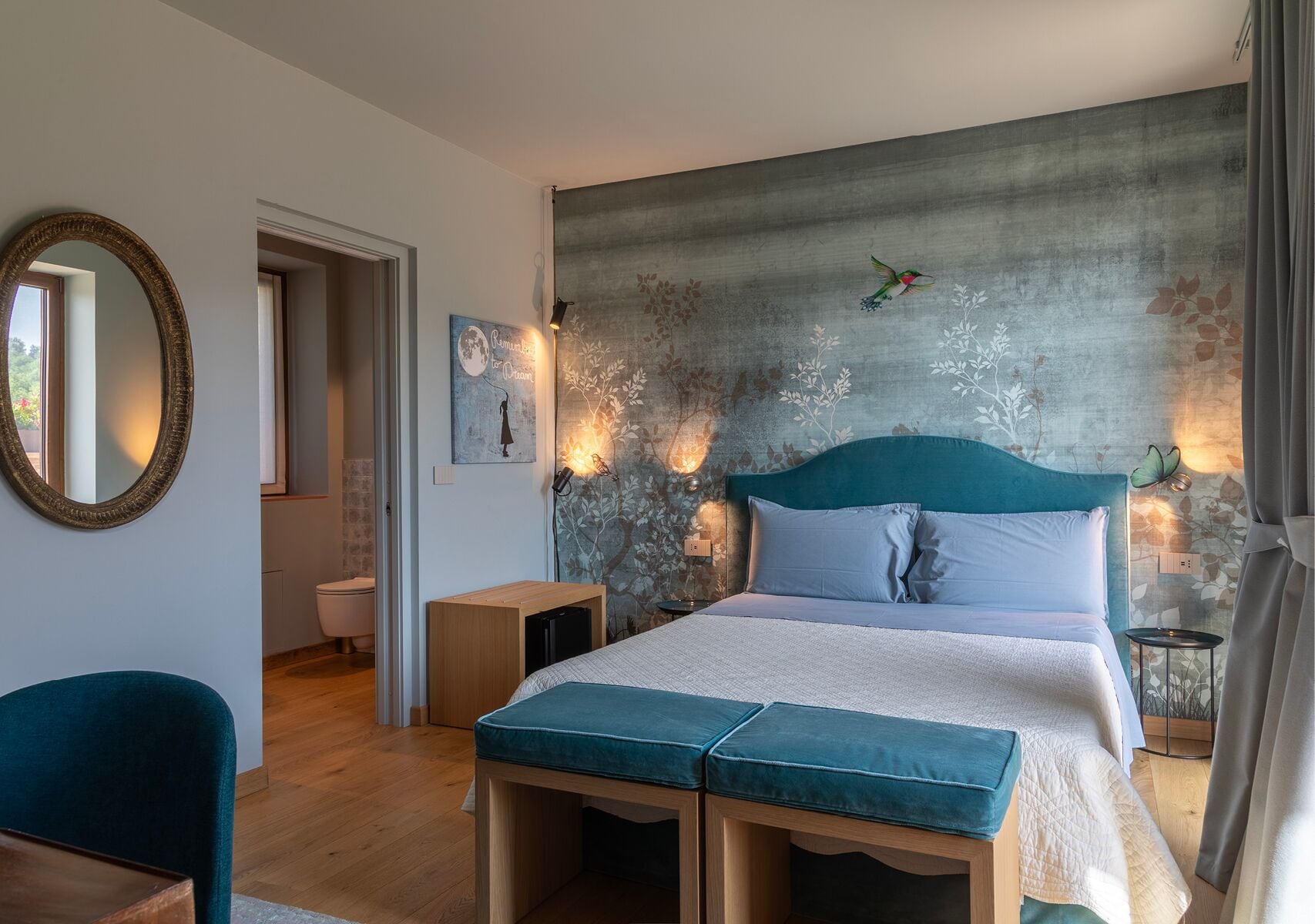 A bedroom with a bed, bedside tables, a mirror, and a wall with a floral mural.