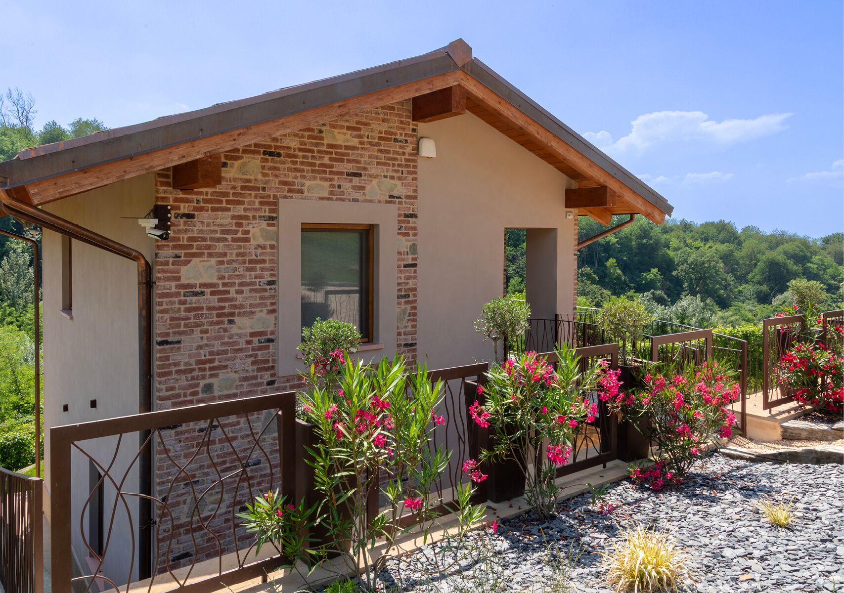 A brick house with a balcony, surrounded by flowering plants and a gravel path.