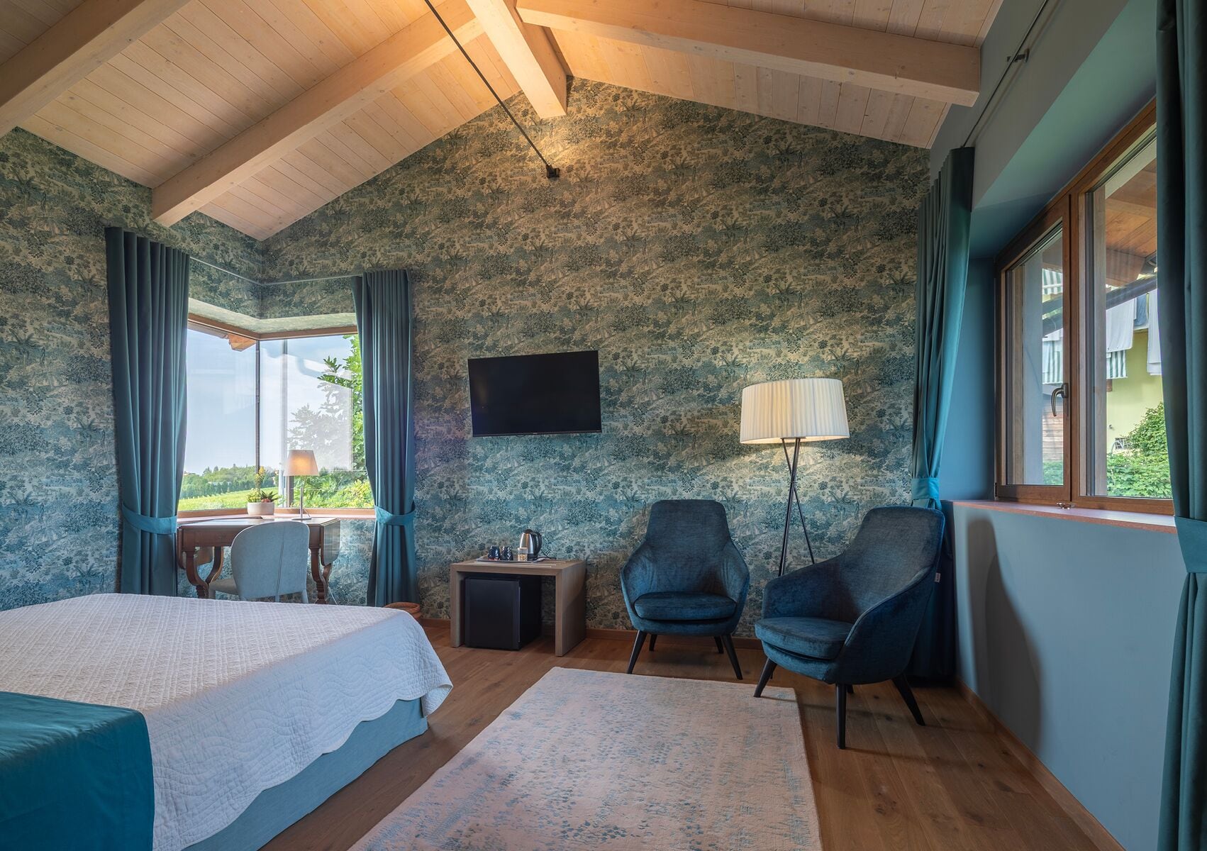 Ein Schlafzimmer mit einem Bett, zwei Stühlen, einem Schreibtisch, einer Lampe und einem Fernseher.