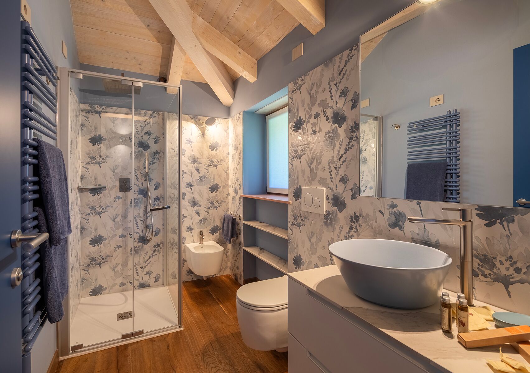Un baño moderno con ducha envuelta en vidrio, un lavamanos tipo recipiente y un inodoro.
