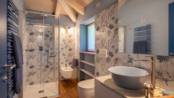 A modern bathroom with a glass-enclosed shower, a large vessel sink, and a toilet.