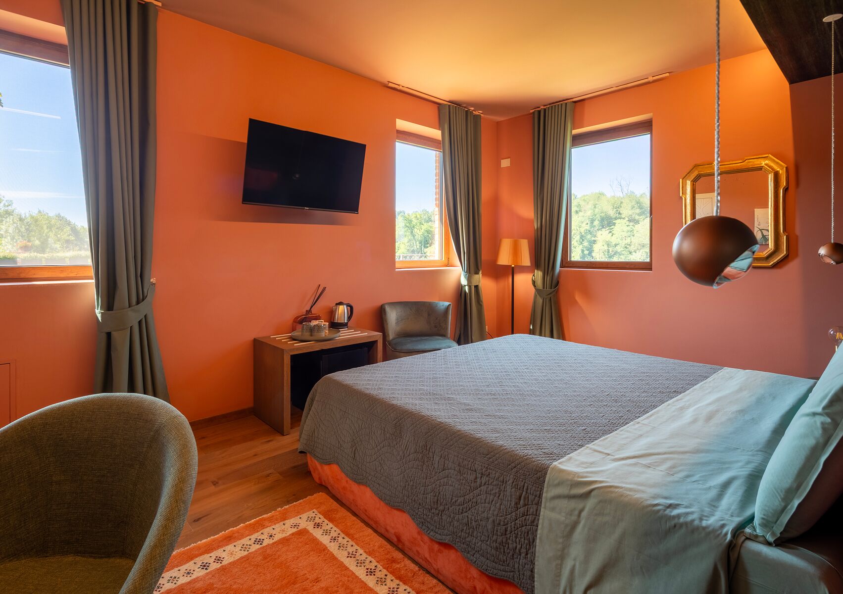 Hotellihuone, jossa on suuri sänky, seinälle asennettu televisio, työpöytä lampun kanssa ja tuoli.