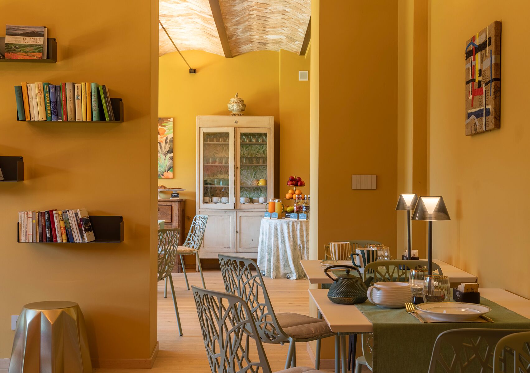 A dining area with a table set for two, chairs, a cabinet with glass doors, and a bookshelf with books.