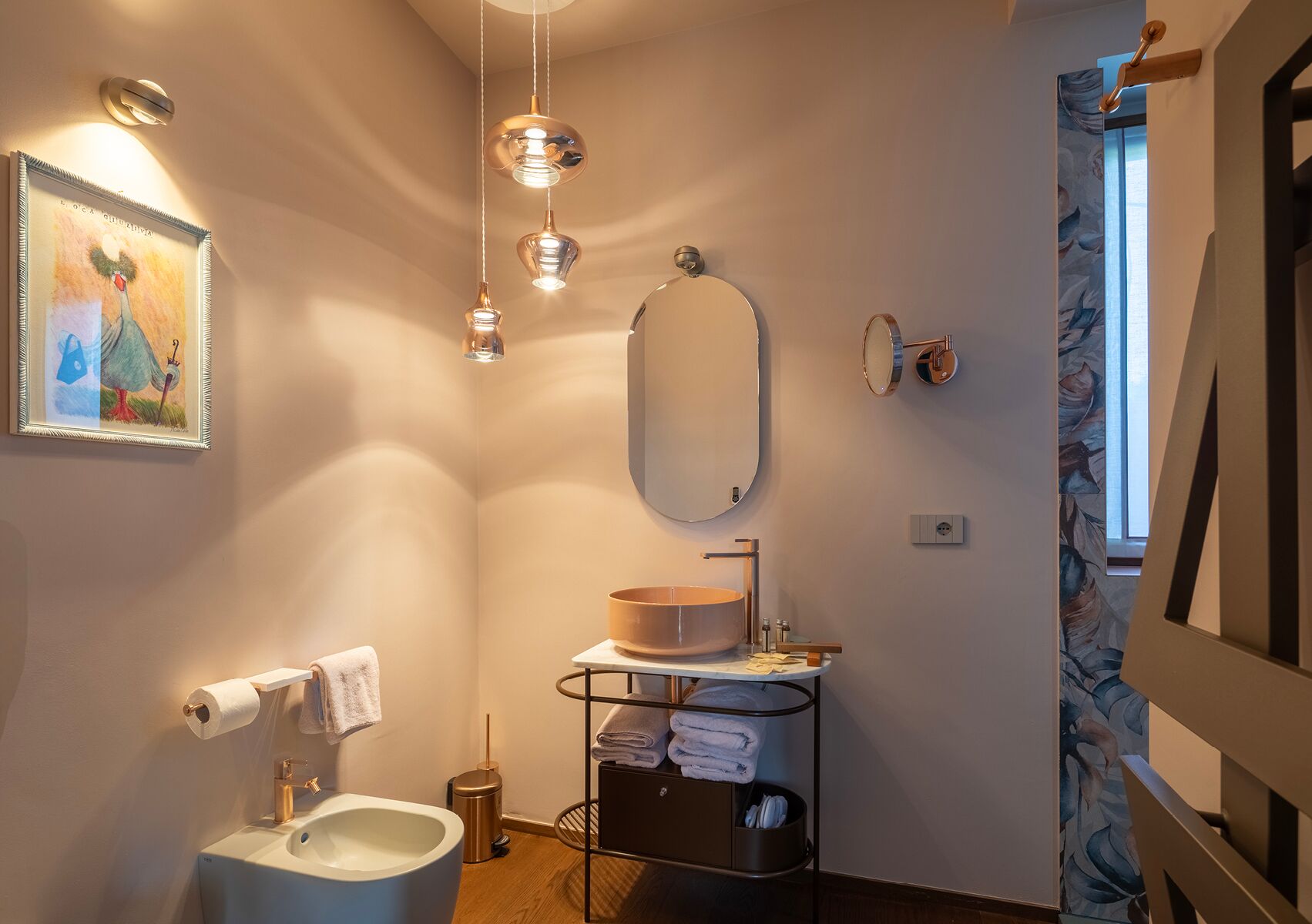 Un baño moderno con inodoro, lavamanos y perchero. Hay un cuadro en la pared y un espejo sobre el lavamanos.