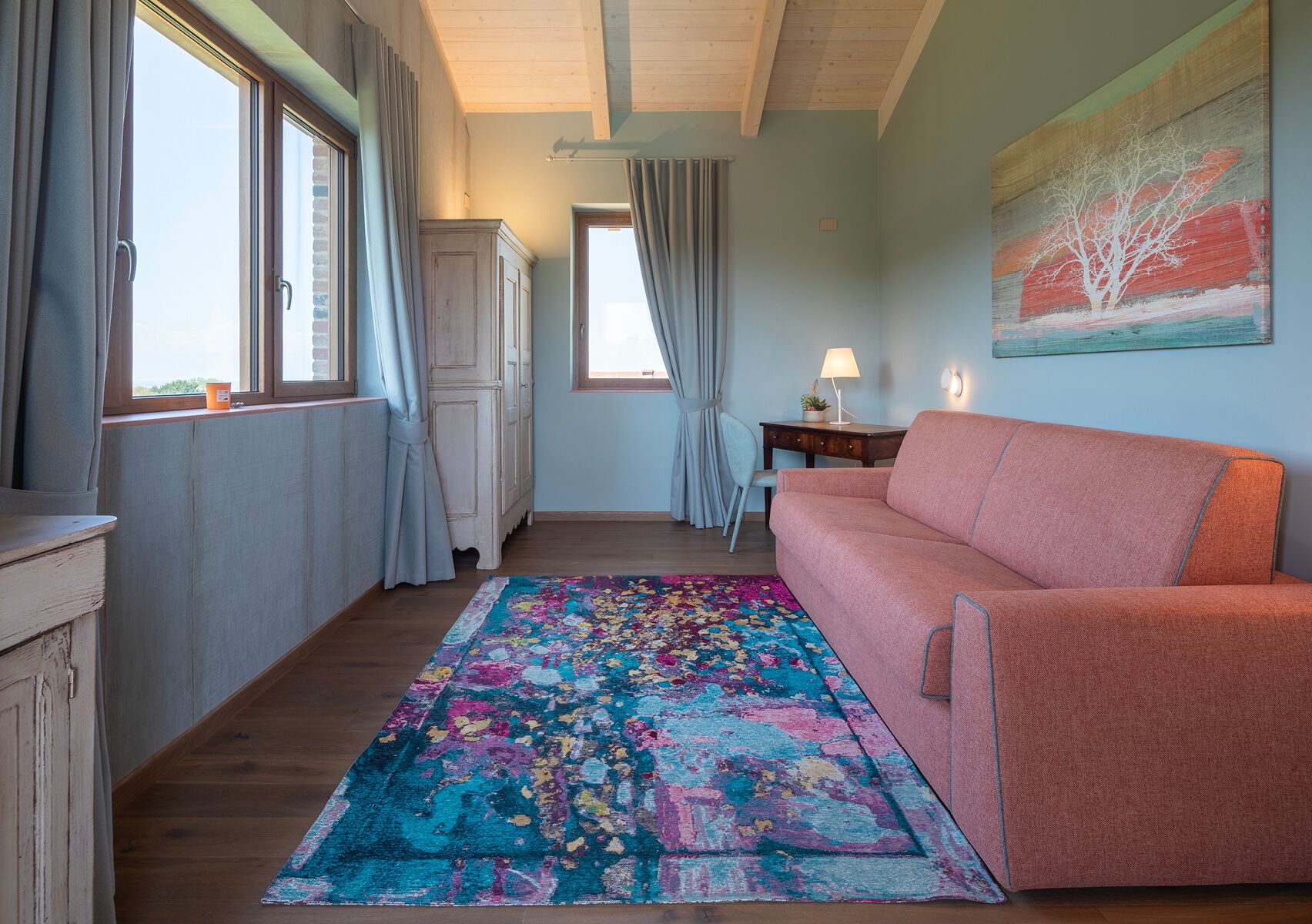 Un cuarto acogedor con un sofá rosa, una alfombra colorida y un cuadro de un árbol.