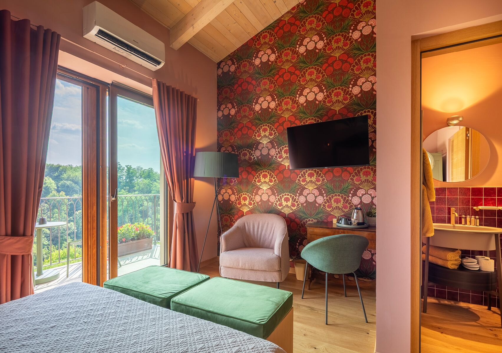Un dormitorio con una cama grande, un reposapiés verde, una silla, un escritorio y un televisor montado en la pared.