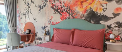 Habitación de hotel con una cama grande, un escritorio y una silla. Hay una ventana con cortinas y una pared con un mural floral.