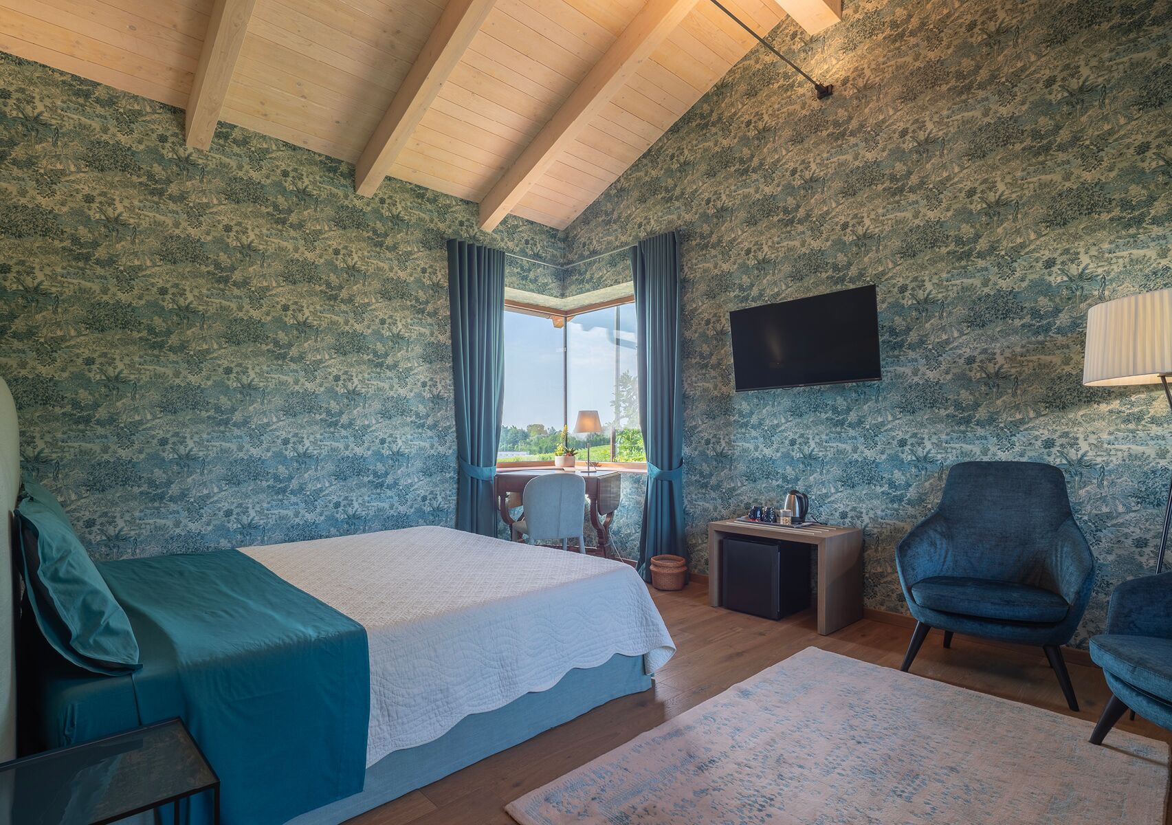 Ein Schlafzimmer mit Bett, Sessel, Fernseher und Blick ins Freie.