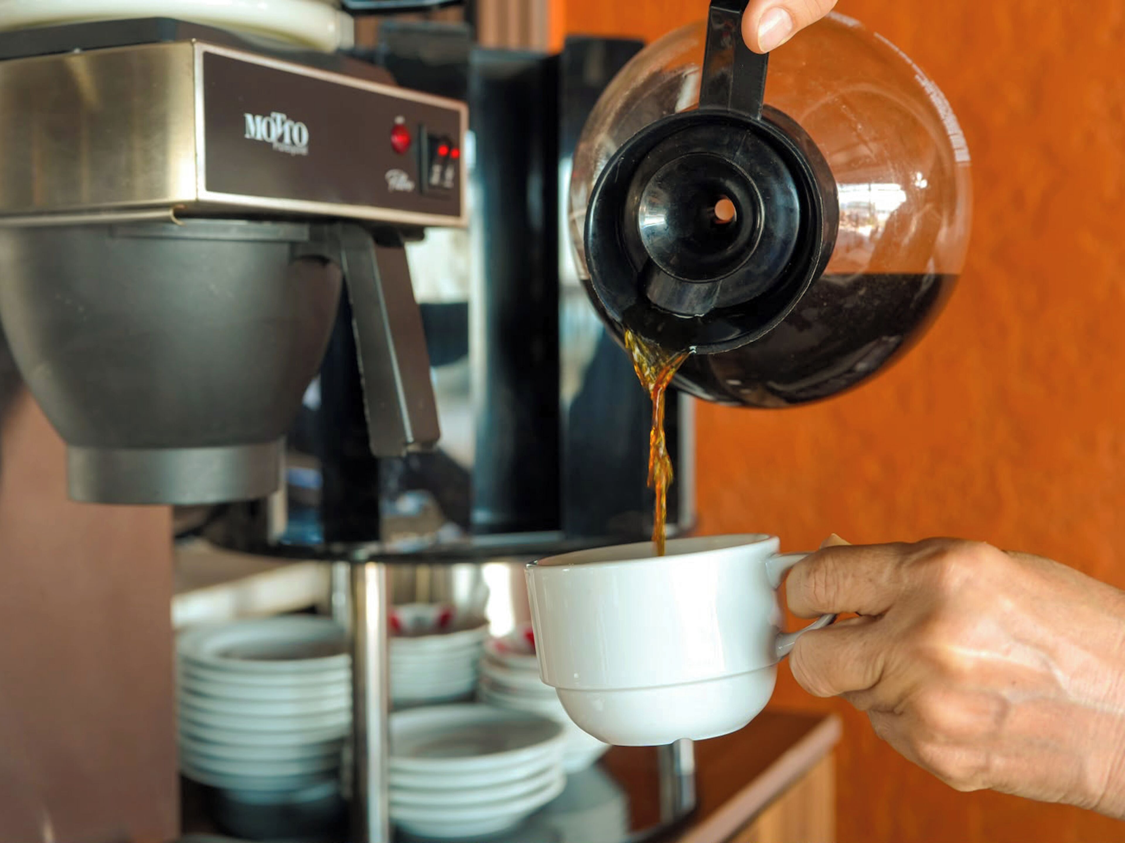 A hand pouring coffee from a machine into a cup.