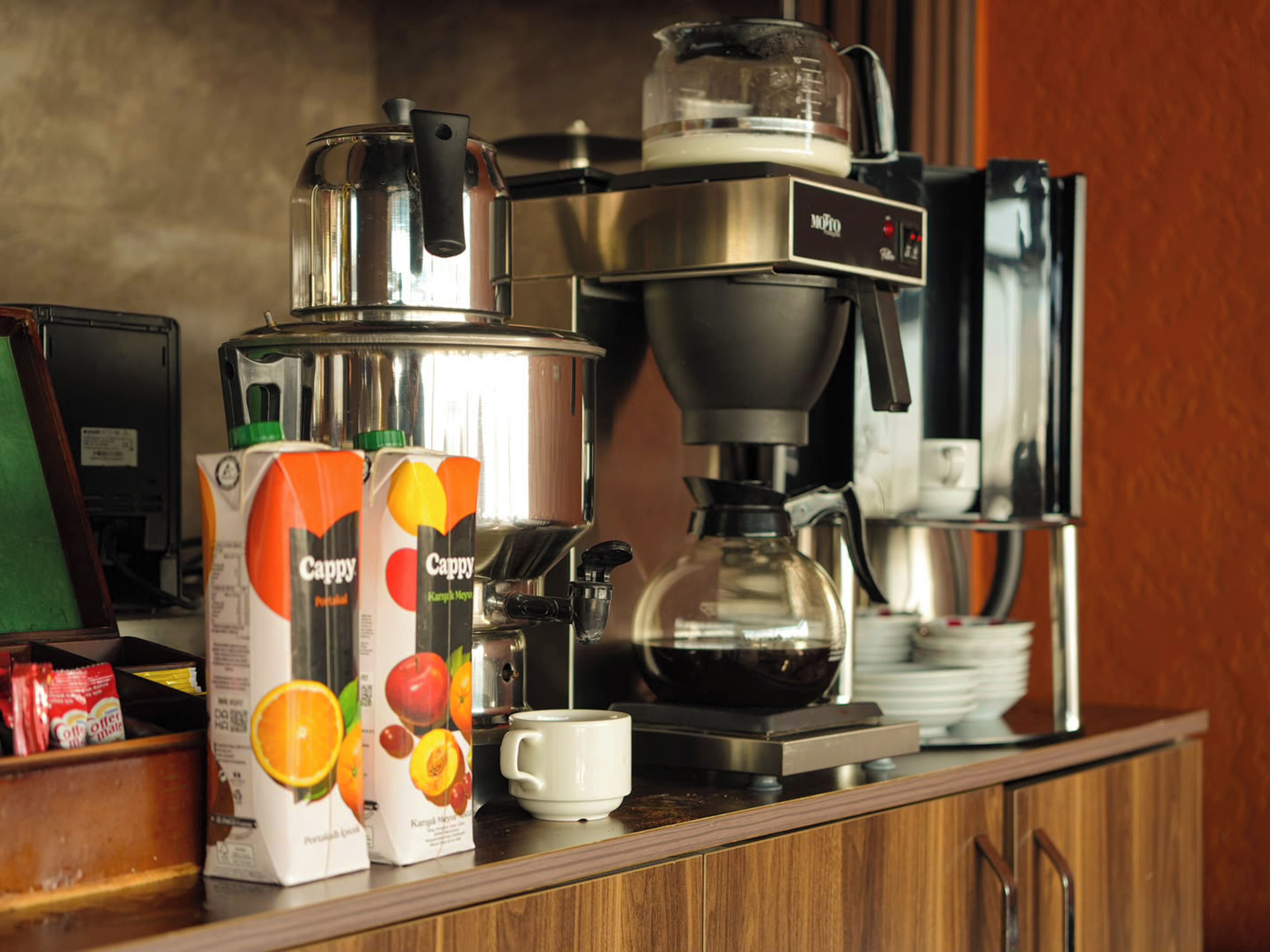 A coffee machine, a milk frother, and two cartons of Cappy juice on a kitchen counter.